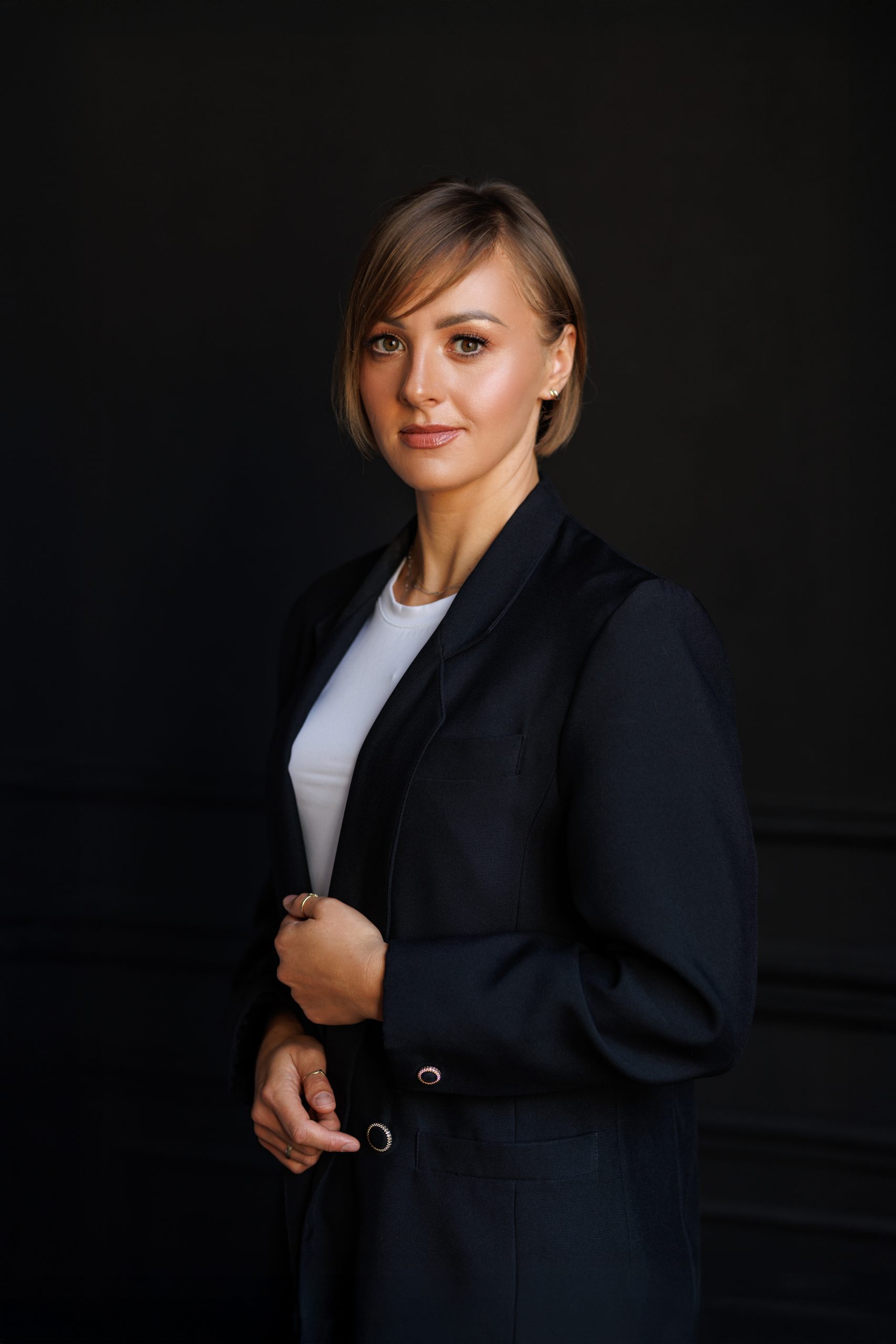 Kobieta w białej bluzce i ciemnym marynarce na czarnym tle.